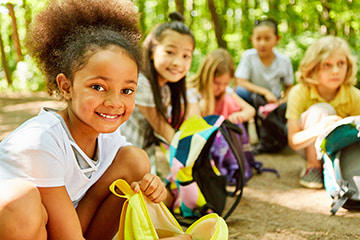 children with backpacks smile in a field